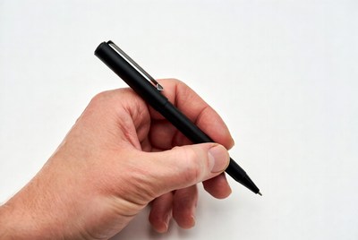 Hand holding a black pen on white surface