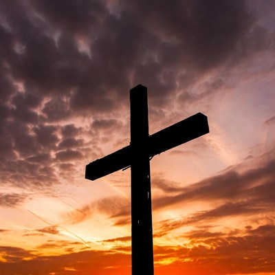 Cross silhouette at sunset over clouds
