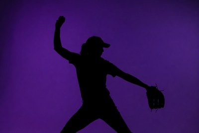 Female pitcher throws a baseball in silhouette