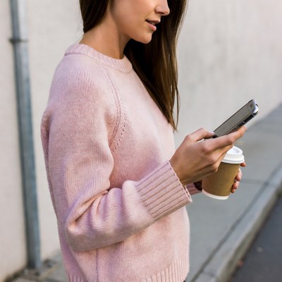 Woman checking phone holding coffee