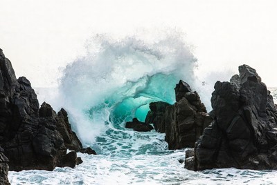 Massive turquoise wave crashing on rocks