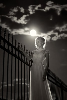 Woman in lace gown by fence under full moon