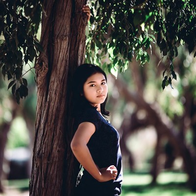 Asian woman leaning against tree