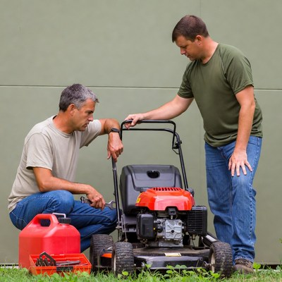 Two men repairing lawnmower outdoors