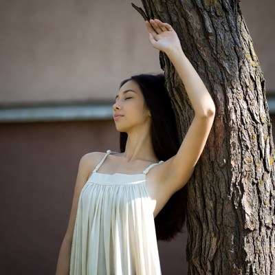 Asian woman leaning against tree