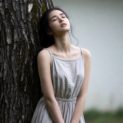 Asian woman leaning against tree