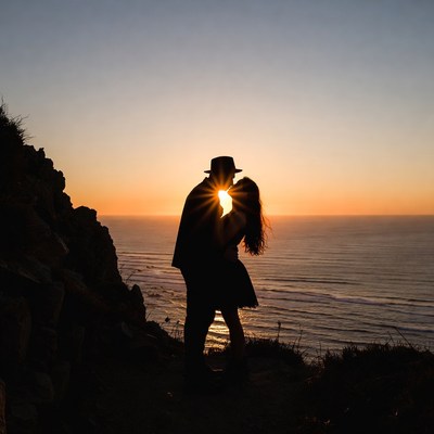Silhouette couple kissing at sunset cliff