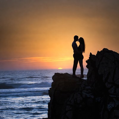 Silhouette couple kissing at sunset cliff