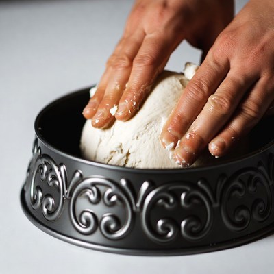 Hands kneading dough in cake pan