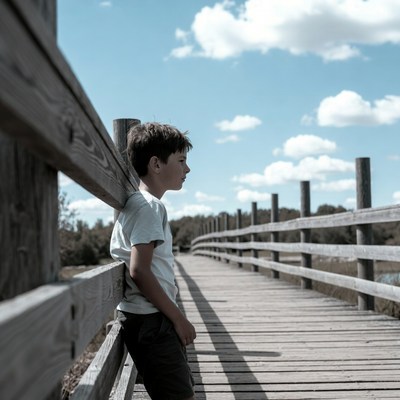 Boy leaning on wooden bridge railing