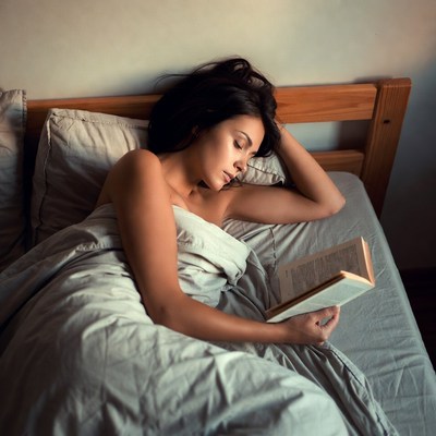 Nude woman reading book in bed