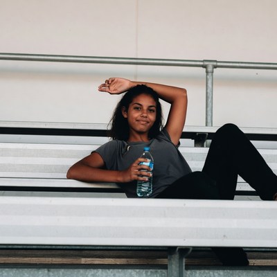 Young Black woman holding water bottle on bleachers