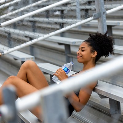 Black woman drinking water on bleachers