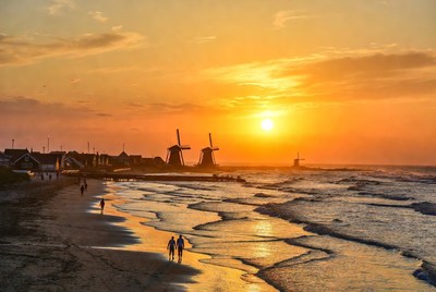 Couple walking beach at sunset with windmills