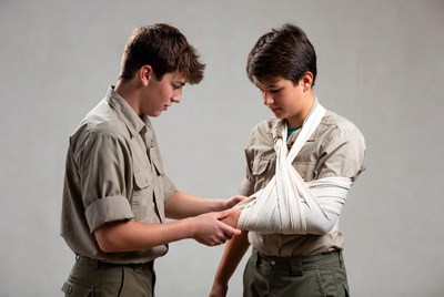 Boy bandaging friend's arm in scout uniforms
