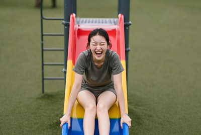 Asian woman sliding down playground slide
