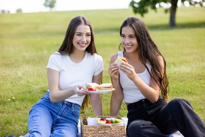 Two women eating sandwiches picnic outdoors