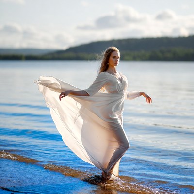 Woman in flowing white dress wading lake