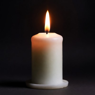 Burning white candle on black background