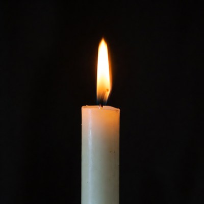 Burning white candle on black background
