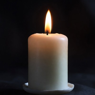 Burning white candle on black background