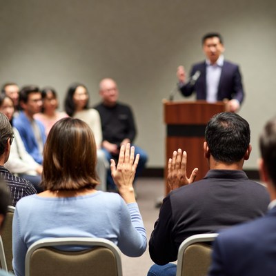 Asian man speaking at conference with raised hands audience