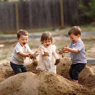 Three toddlers playing in sand pile
