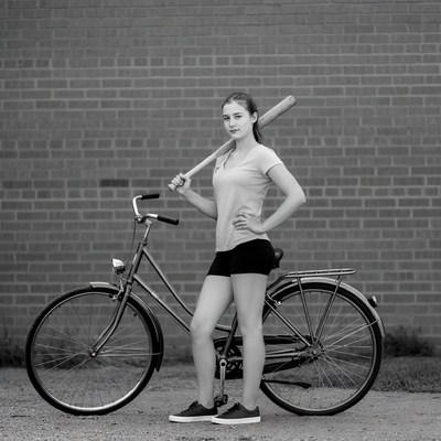 Girl with bat standing by bicycle