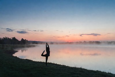 Woman doing yoga pose by lake sunset
