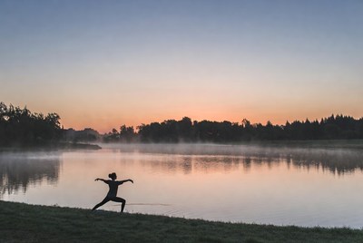 Woman doing yoga by misty river sunrise