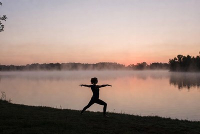 Woman doing yoga silhouette at sunset lake