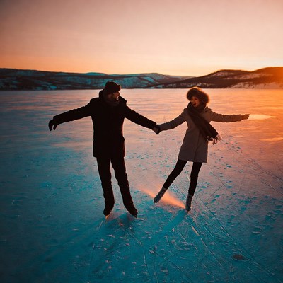 Couple ice skating on frozen lake at sunset