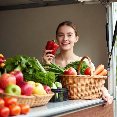 Smiling woman holding red bell pepper at vegetable stand