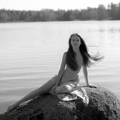 Nude girl sitting on rock by lake