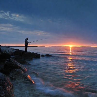 Man fishing at sunset by seaside