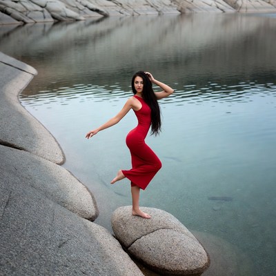 Woman in red dress posing on rock by lake