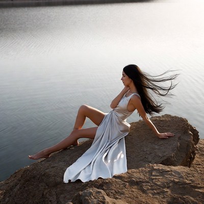 Woman in white dress on lakeside rock
