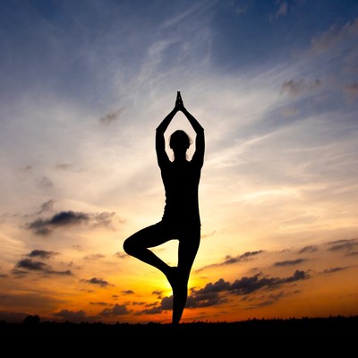 Woman in yoga tree pose silhouette sunset