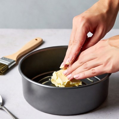 Woman greasing cake pan with butter