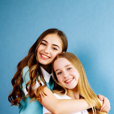 Two girls hugging on blue background
