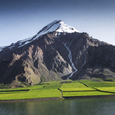 Snow-capped mountain over green fields lake