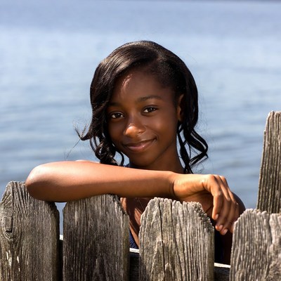 African-American girl leaning on wooden fence by lake