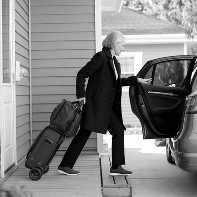 Elderly woman loading suitcase into car