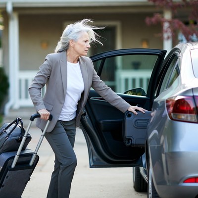 Elderly woman loading suitcase into car