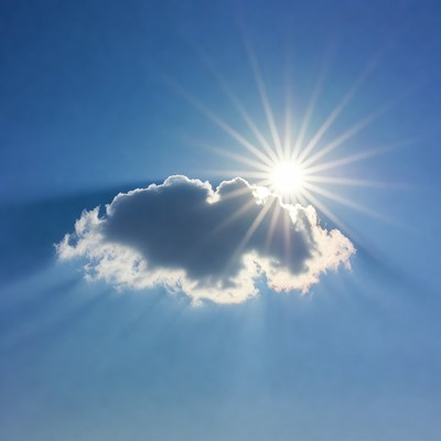 Sun behind fluffy cloud in blue sky
