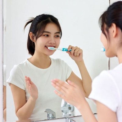Asian woman brushing teeth in mirror