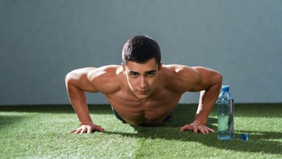 Muscular man doing pushups on grass