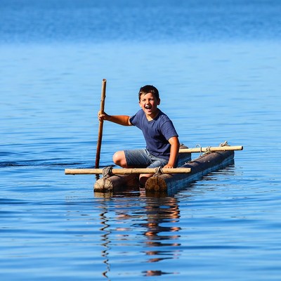 Boy paddling bamboo raft on lake