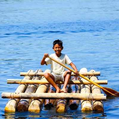 Asian boy paddling bamboo raft