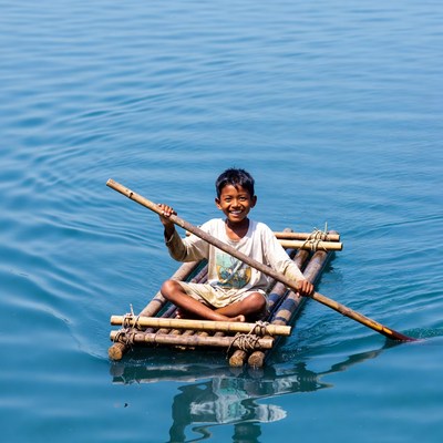 Asian boy paddling bamboo raft